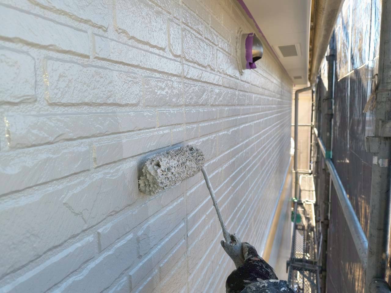 上塗りをした白い外壁に塗装を塗り重ねる